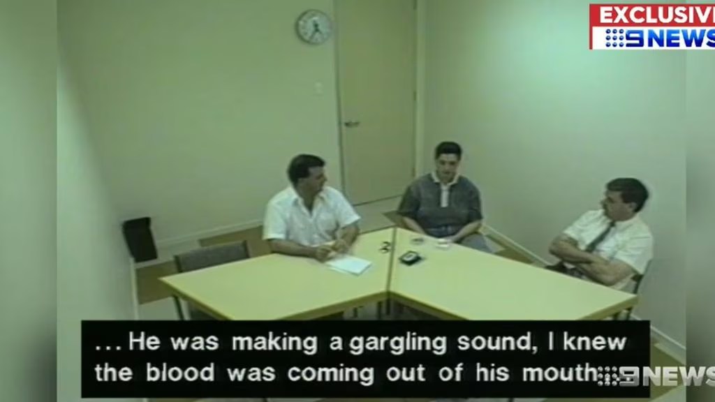 A police interrogation room with three men seated at a table. One man in a white shirt is speaking, while the others listen intently. Subtitles at the bottom describe a traumatic event.