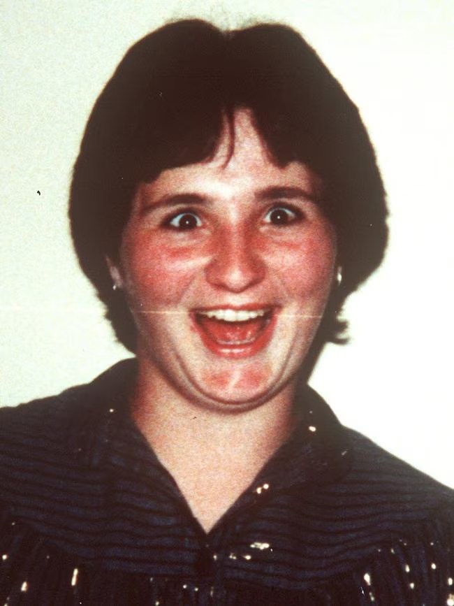 A woman smiling broadly with a playful expression, wearing a dark shirt with stripes.